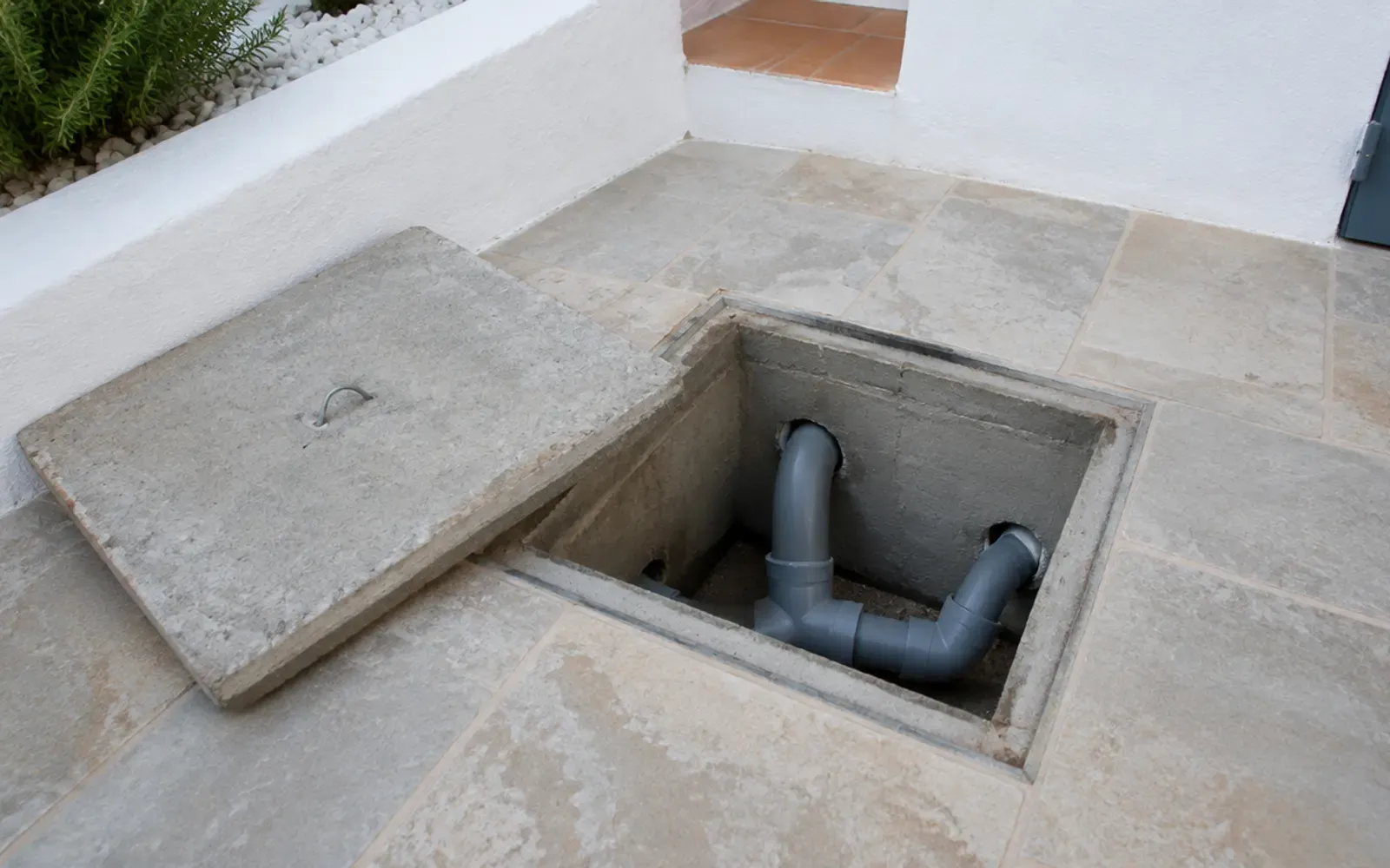 Arqueta de registro abierta en un patio encalado, con las tuberías de desagüe a la vista
